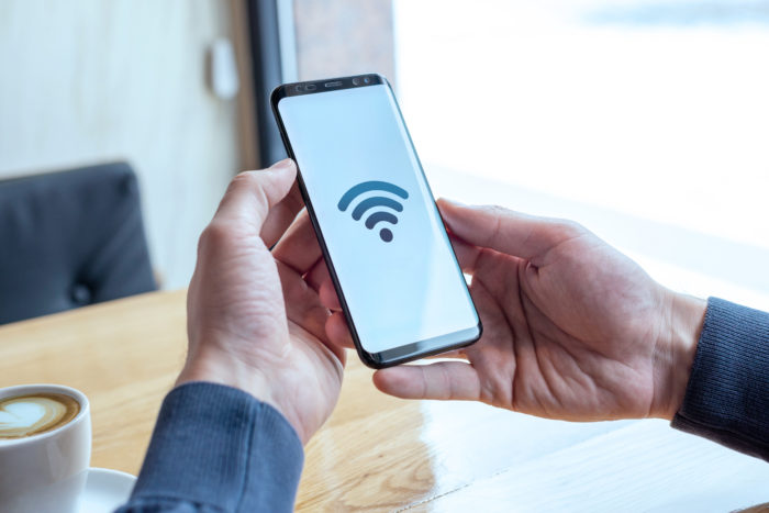 Ícone do conceito Wi-fi na tela do telefone inteligente. Mãos segurando um celular na cafeteria. O conceito de internet gratuita e conexão global